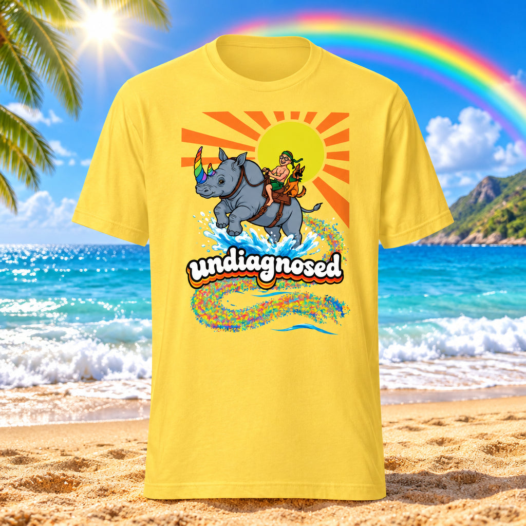 A yellow short-sleeve crewneck t-shirt featuring a colorful graphic print of a man riding a rhinoceros with a rainbow horn, set against a yellow sunburst and below the text 'undiagnosed' in a rainbow pattern.